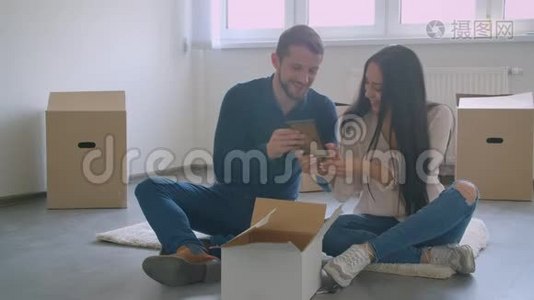 年轻的白种人夫妇坐在新房子的地板上，选择了相框照片的位置。视频