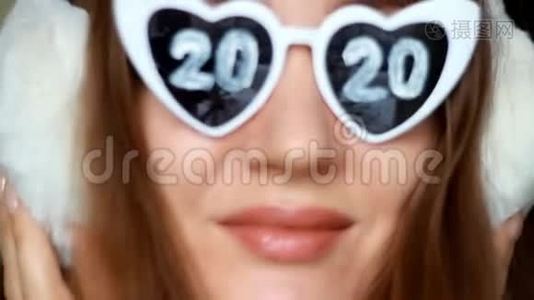 戴眼镜的女人戴着2020年的数字和冬天的耳机。 新年。 圣诞节。 女孩微笑着看着镜头视频