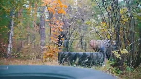 一个戴着手套的纹身男健美运动员推着卡车轮胎在地上-在秋天的森林里训练视频