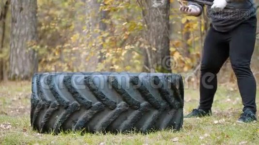 一位身材魁梧的健美运动员用锤子砸在卡车轮胎上-秋天的森林视频