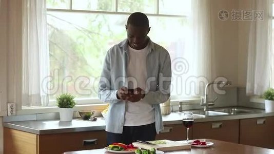 快乐的非洲男人使用智能手机手机应用程序烹饪厨房视频