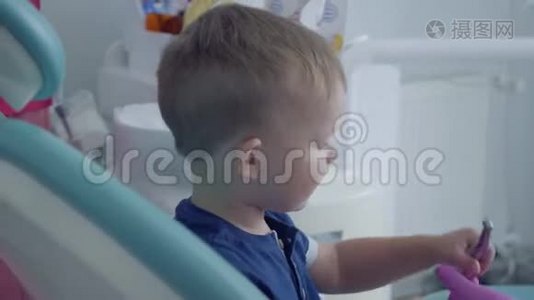 爱的牙医用双手检查坐在椅子上的无忧无虑的小男孩的牙齿，给他看一张镜子特写视频