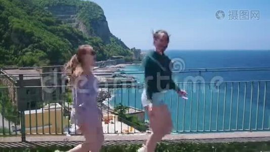 两个年轻快乐的女人在海城背景下的观景台上散步视频