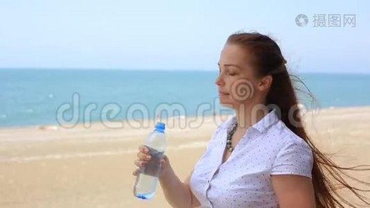女人从海滩上的瓶子里喝水。视频