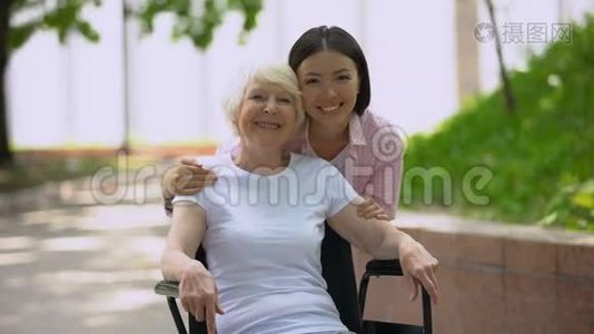 年轻女子抱着奶奶坐在轮椅上，看着室外的摄像机视频