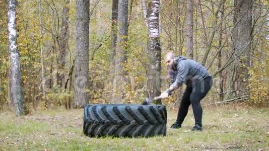 一个强壮的健美男子用金属锤击卡车轮胎-秋天的森林视频