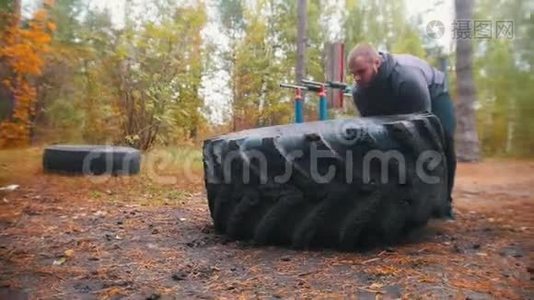 一个纹身的强壮的健美男子推着轮胎在地上-训练在秋天的森林视频