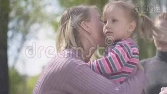 肖像金发年轻女子拥抱和亲吻她的女儿在阳光下近距离。 家庭幸福。 母亲和她的孩子视频