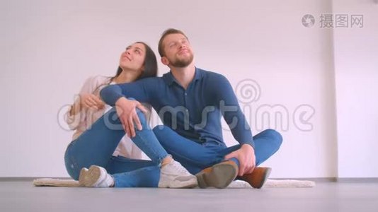 年轻的白种人夫妇坐在新的空的地板上，平抱，亲吻，在白色的墙壁背景下快乐视频