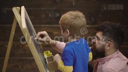 一个男孩和留胡子的人的特写，他用粉笔在黑板上写字。 侧视学生和教师面前视频
