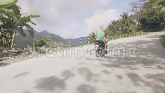 在青山覆盖热带雨林的蜿蜒公路上驾驶摩托车的老人。 成人男子旅行视频