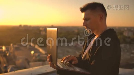 一个有笔记本电脑的程序员坐在屋顶上，在日落时写代码。 远程工作自由职业者。 工作自由。 打字视频