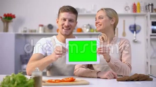 年轻的微笑夫妇展示绿色屏幕平板电脑，烹饪课程模板视频