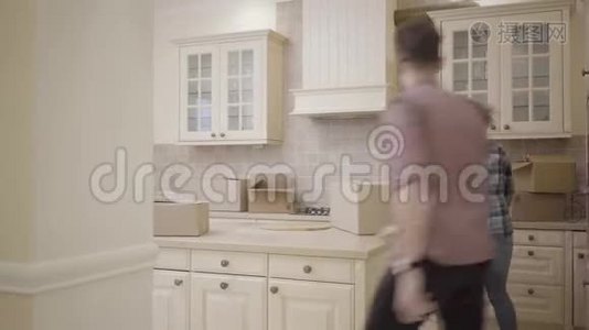 开朗的男人在厨房里追女人，男人追他的妻子，然后抓住她。 盒子掉在地板上。 丈夫视频