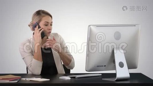 迷人的年轻女子在手机上说话，微笑着坐在办公室的工作场所，看着她视频