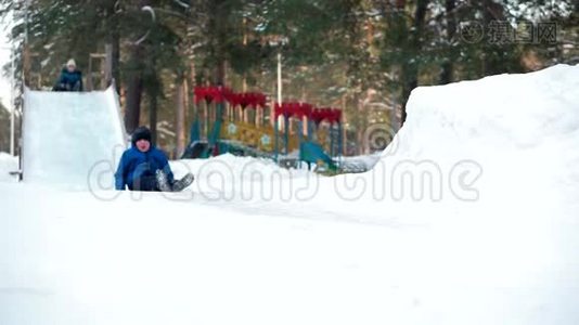 在冬季公园里，男孩坐着雪橇和木制过山车。视频