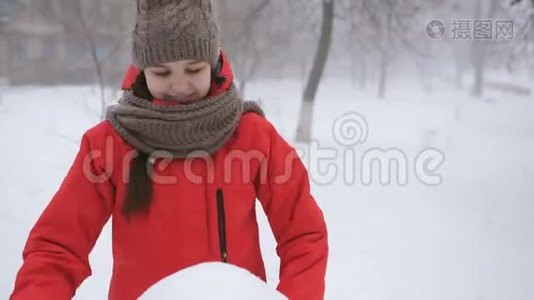 穿着红色kopcke的少女在街上雕刻一个雪人。视频