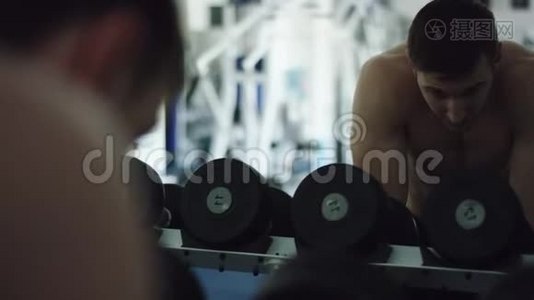 年轻强壮的男人在健身房里对着镜子看哑铃视频