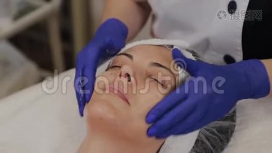 专业美容师用擦洗油涂在女人的脸上，用她的手按摩。视频