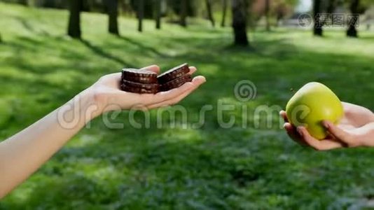 手选择吃什么绿色苹果或巧克力烘焙。 背景中有公园，天气晴朗.. 的概念视频