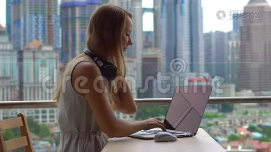 年轻女性自由职业者在她的笔记本电脑上工作，在一个阳台上的手机上交谈，背景是视频