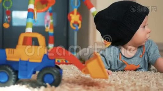 可爱的小男孩戴着帽子，玩具躺在家里的地板上。视频