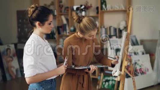 年轻的女学生正在用油画画画布，而她有经验的老师则站在她身边视频