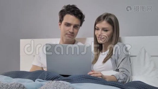 幸福的年轻夫妇在床上使用笔记本电脑视频