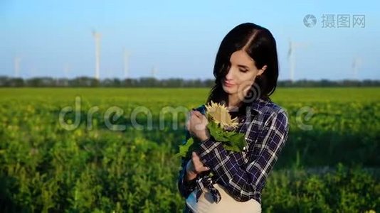 一个年轻漂亮的女人站在一片向日葵的田野里，微笑着欣赏着这朵花。 慢动作视频