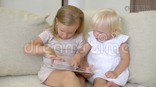 两个孩子在家用平板电脑看ang。 儿童使用现代笔记本电脑，平板电脑在沙发上。 小女孩在玩视频