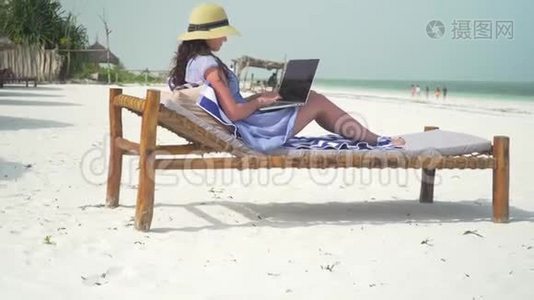 年轻女子在海边的白色沙滩上使用笔记本电脑视频