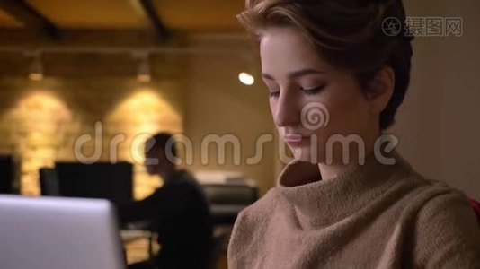 年轻的短发女人在办公室里专心地用笔记本电脑工作的特写肖像。视频