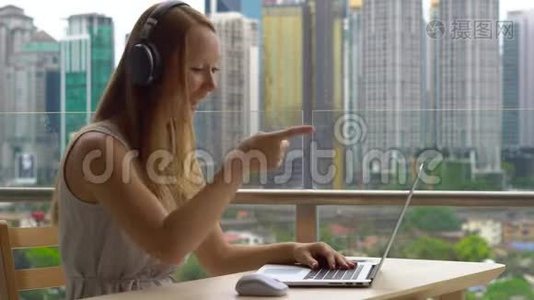 年轻女性自由职业者在阳台上的笔记本电脑上工作，背景是一个充满摩天大楼的市中心。 远程视频