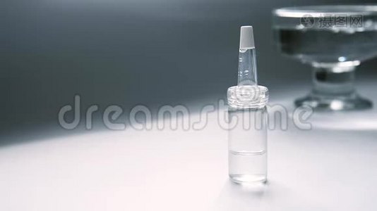 一个装有乳清的吸管的玻璃瓶在桌子上，玻璃容器的背景是水的摇摆。视频