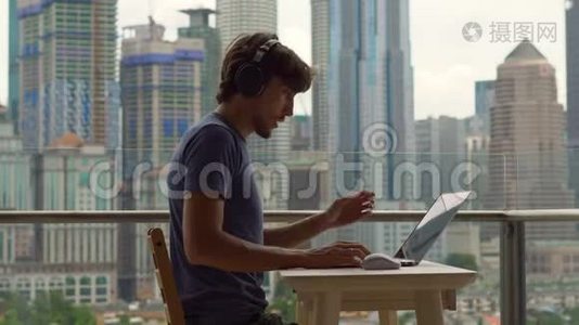 年轻的自由职业者在阳台上的笔记本电脑上工作，背景是一个充满摩天大楼的市中心。 自由职业者视频