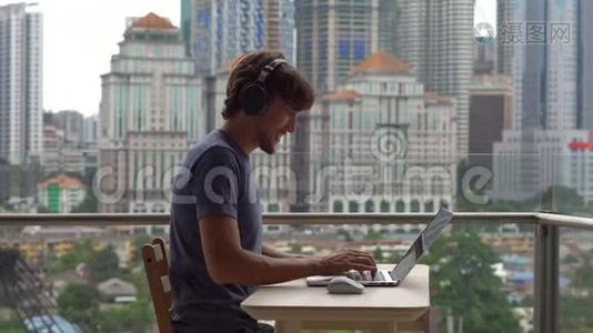 年轻的自由职业者在阳台上的笔记本电脑上工作，背景是一个充满摩天大楼的市中心。 远程视频