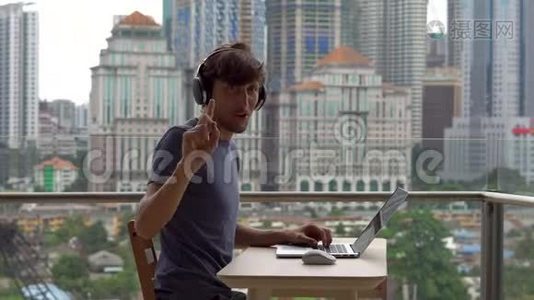 年轻的自由职业者在阳台上的笔记本电脑上工作，背景是一个充满摩天大楼的市中心。 远程视频