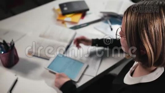 特写女生或学生使用平板电脑并在工作簿中书写。 她`在做作业。视频