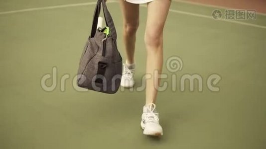 为年轻健康女性提供一个包和网球拍的腿部特写镜头，并为球场上的训练做准备视频