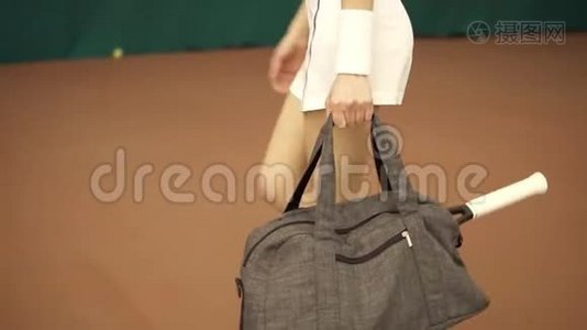为年轻健康女性提供一个包和网球拍的腿部特写镜头，并为球场上的训练做准备视频