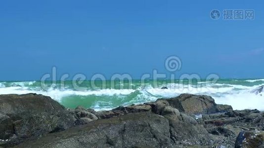 海浪拍打在岩石海滩上的蓝天景观。 关闭海洋中石质海岸的海浪。 蓝色视频