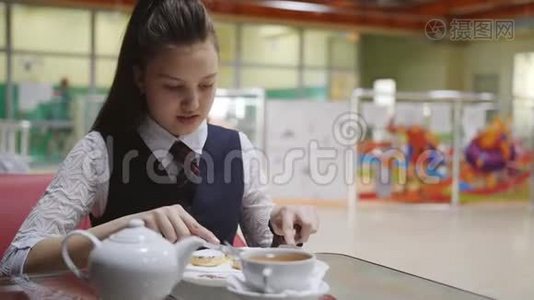 穿着校服的少女坐在学校食堂的桌子旁吃蛋糕，喝茶。视频