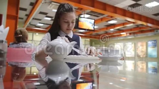 穿着校服的少女坐在学校食堂的桌子旁吃蛋糕，喝茶。视频