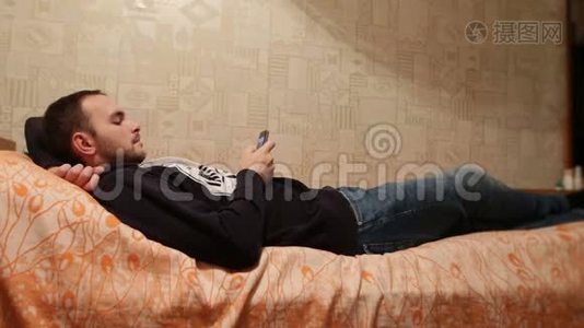 男人躺在家里的床上，在肖像模式下使用手机。 懒惰的白种人在看新闻或照片视频