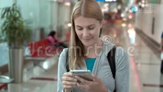 女人在机场候机楼散步。 使用智能手机，浏览，与朋友聊天，阅读新闻视频