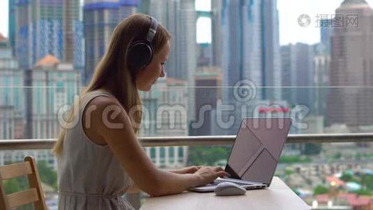 年轻女性自由职业者在阳台上的笔记本电脑上工作，背景是一个充满摩天大楼的市中心视频
