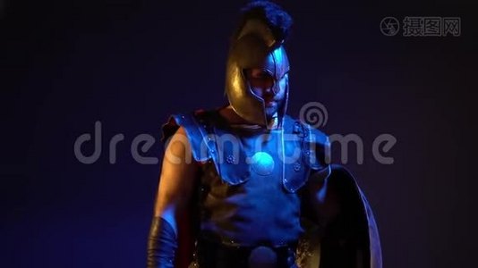 戴着头盔和盔甲，脸上有伤疤的无胡子罗马角斗士用盾牌遮住他的头，挥动他的剑视频