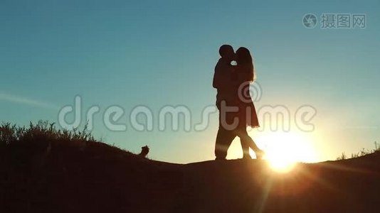 情侣在夕阳下剪影亲吻拥抱.. 慢动作视频。 年轻夫妇在日落时接吻。 男人和女孩见面视频