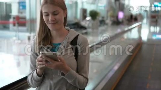在机场候机楼使用牵引器的女人。 在等飞机。 利用她的智能手机浏览视频