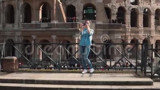 旅游女用智能手机在意大利罗马竞技场拍照。 女孩跑下台阶。 慢动作。视频